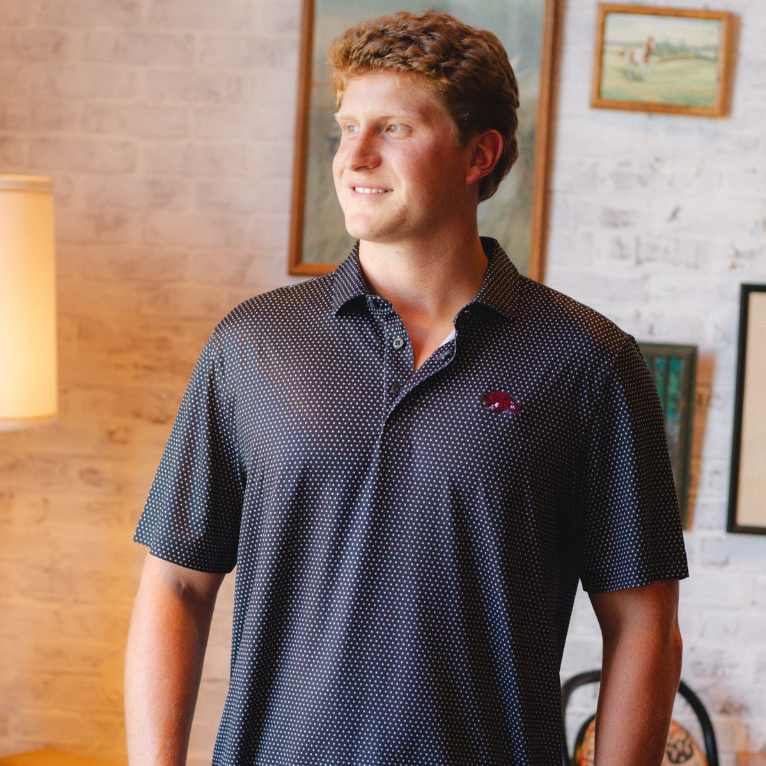 Close-up of a dark Black polo shirt with a white micro-dot pattern and a red embroidered Slobbering Hog Razorback logo on the chest.