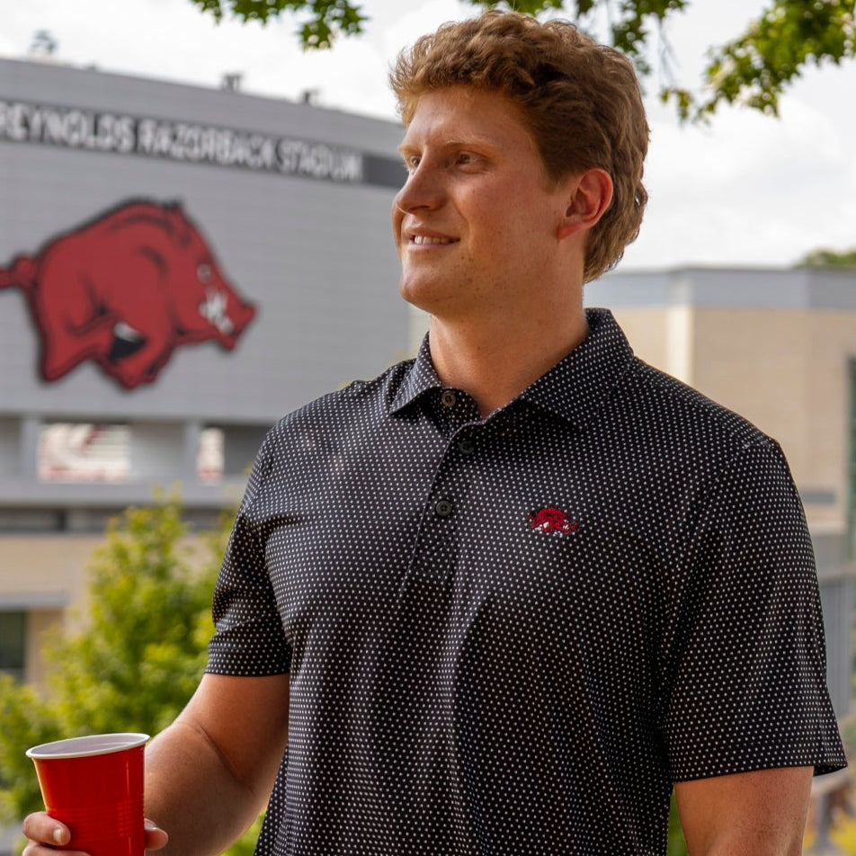 Close-up of a dark Black polo shirt with a white micro-dot pattern and a red embroidered Slobbering Hog Razorback logo on the chest.