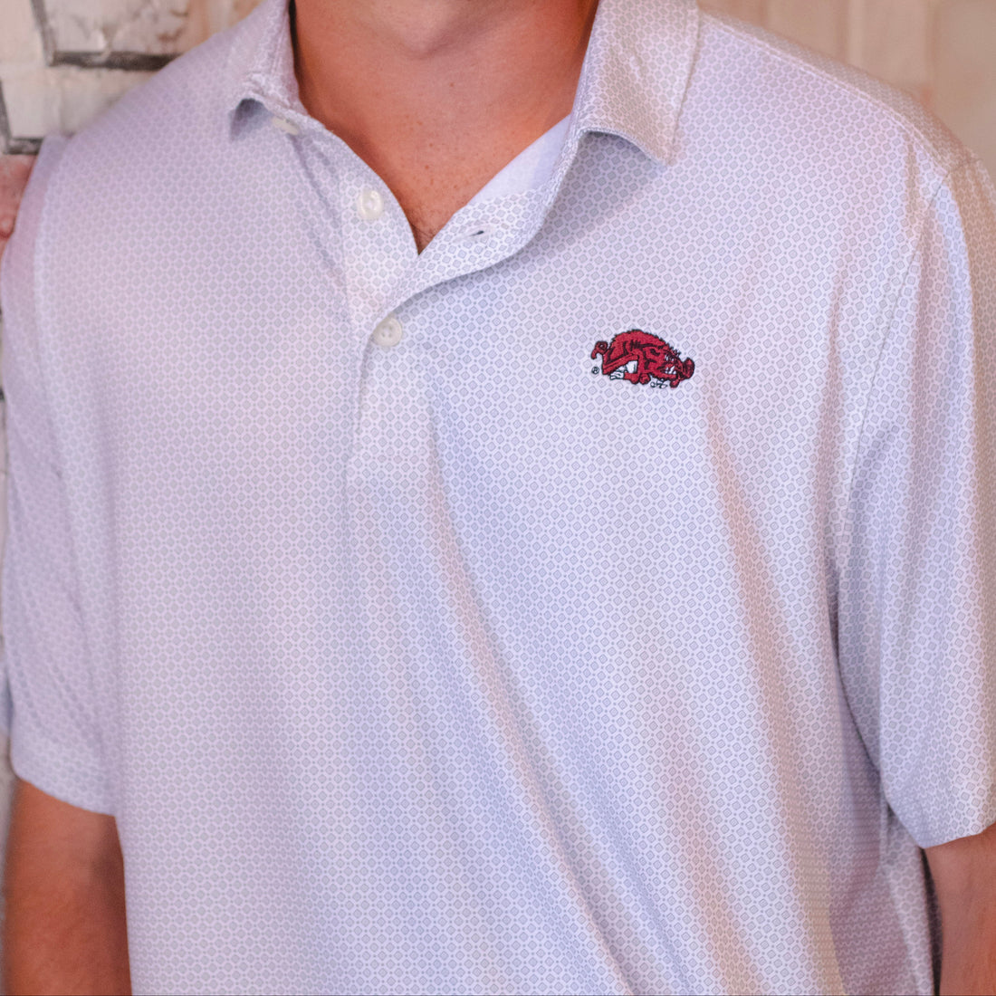 Close-up of a white patterned polo shirt with a red embroidered Arkansas Razorbacks Slobbering Hog logo on the chest 