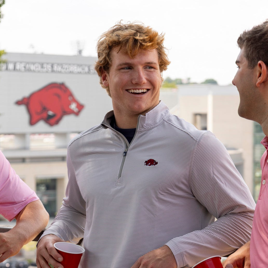 A light pink and white striped long-sleeve quarter-zip pullover with a small red Arkansas Razorbacks logo on the left chest, displayed flat against a cream background.