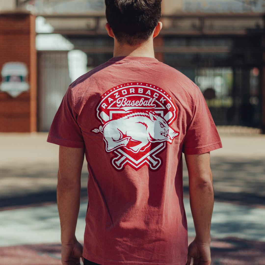 Person wearing a red Houndstooth t-shirt with a 'Razorbacks Baseball' logo on the back, standing outside Baum Walker Stadium.