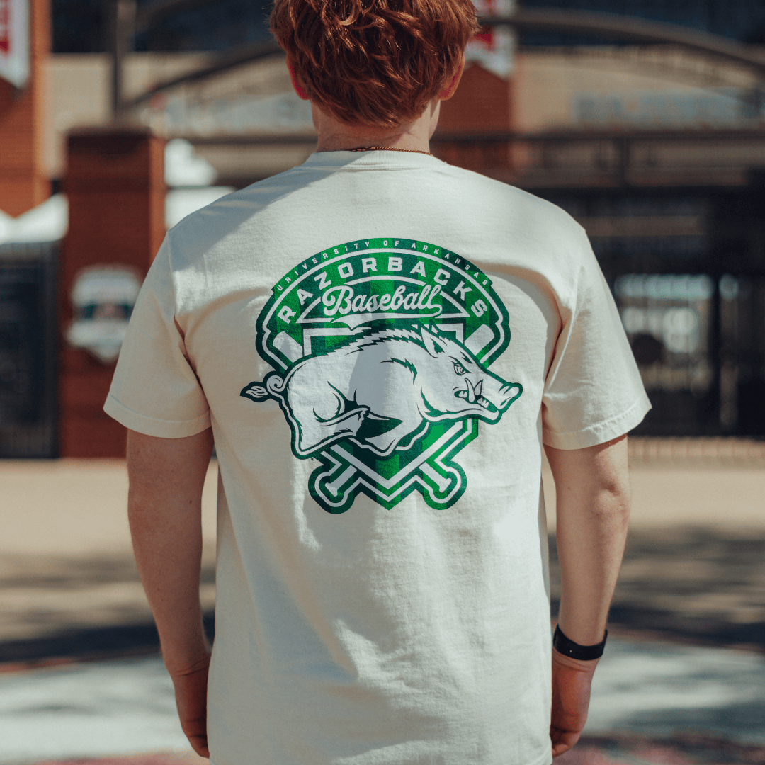 Person wearing an ivory Houndstooth t-shirt with a 'Razorbacks Baseball' logo on the back, standing outside Baum Walker Stadium.