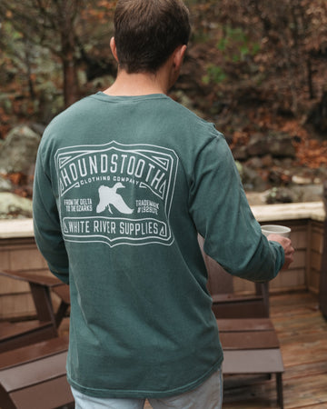 Person wearing a green long-sleeve shirt with a mallard duck, standing on a wooden deck with a forest background.