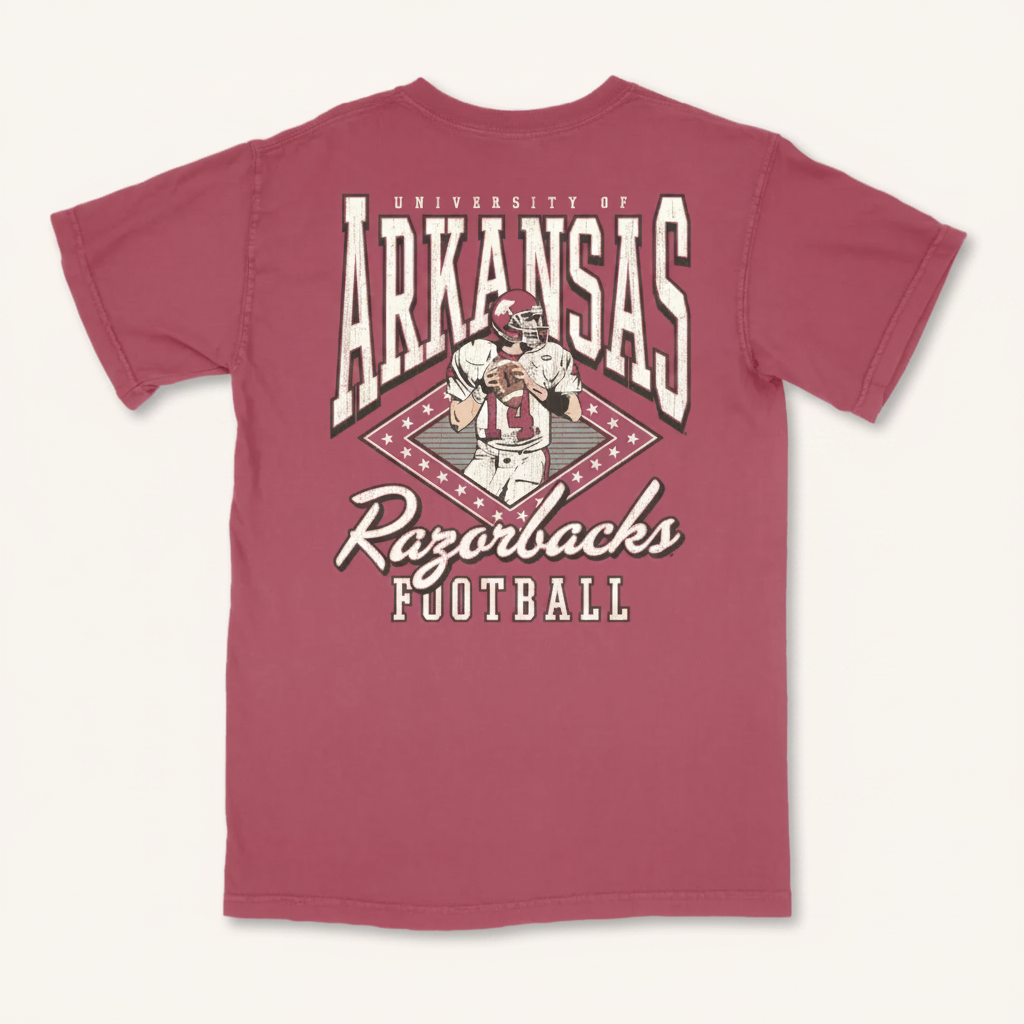 A maroon short-sleeve t-shirt with a large back graphic featuring the text 'University of Arkansas Razorbacks Football' and an illustration of a football player, shown on a plain white background.