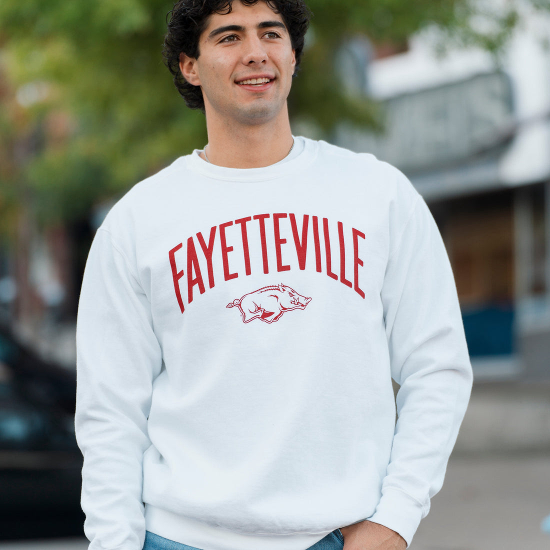 Person wearing a white Houndstooth sweatshirt with 'FAYETTEVILLE' and a Tusk Running Razorback logo, standing outdoors.