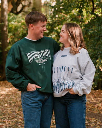 Two people standing outdoors amongst falling autumn leafs in Fayetteville, AR, wearing Houndstooth crewneck sweatshirts.