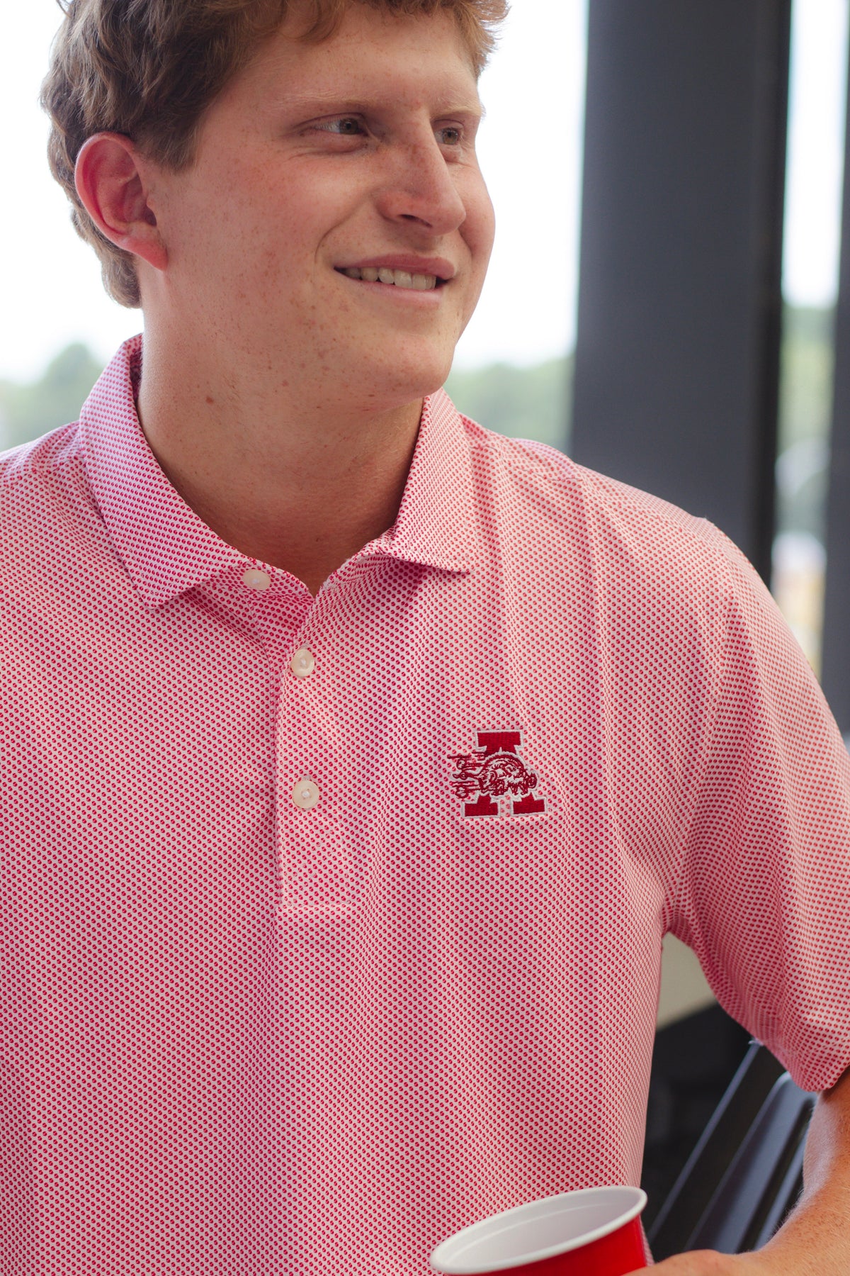 Markham Symmetry Polo in Red on a balcony overlooking Razorback Stadium