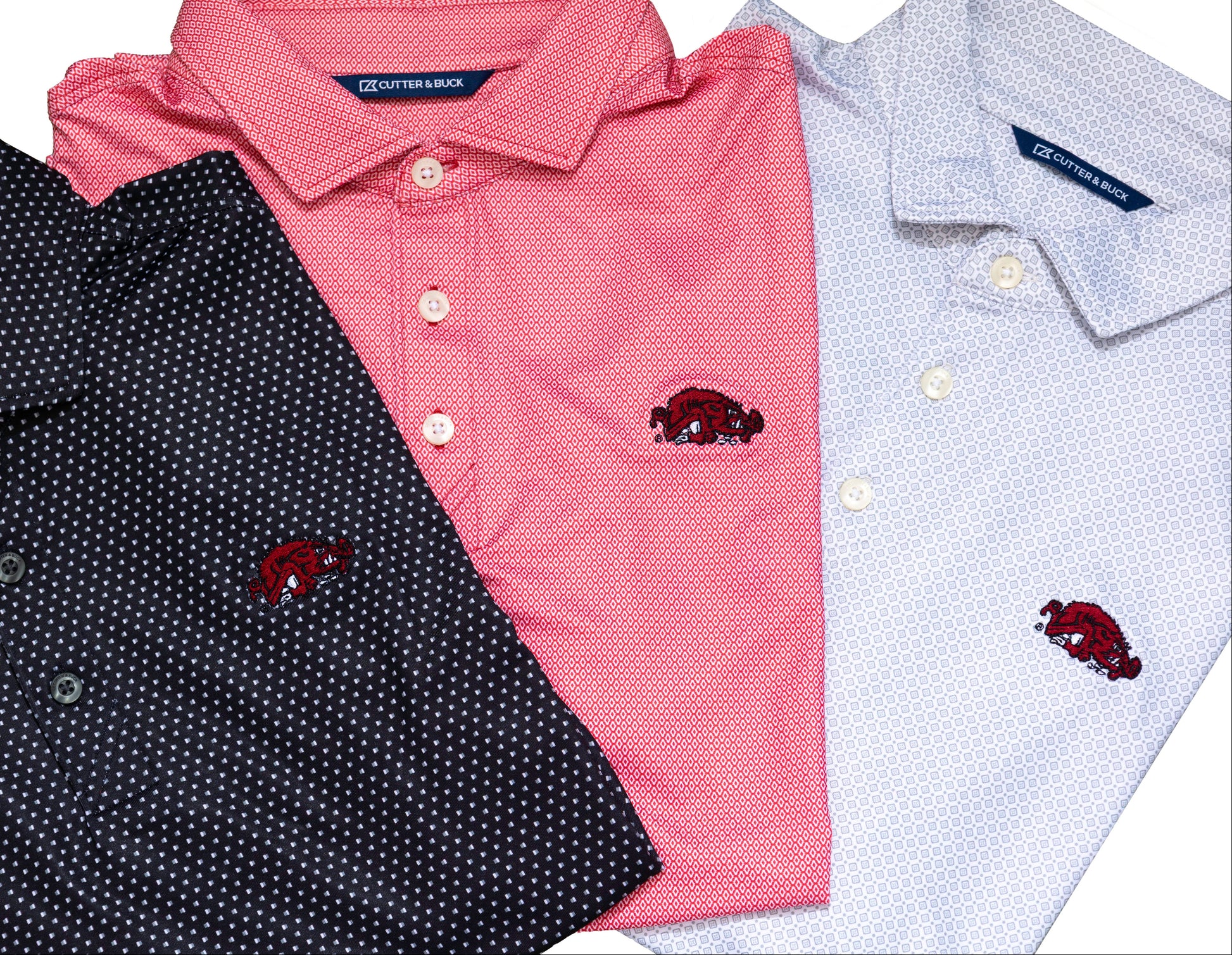 Three folded short-sleeve polo shirts shown on a white background: a dark black shirt with small white dots, a red shirt, and a light grey shirt with a subtle white dot pattern. Each shirt has a small embroidered red Razorback basktball logo on the chest.