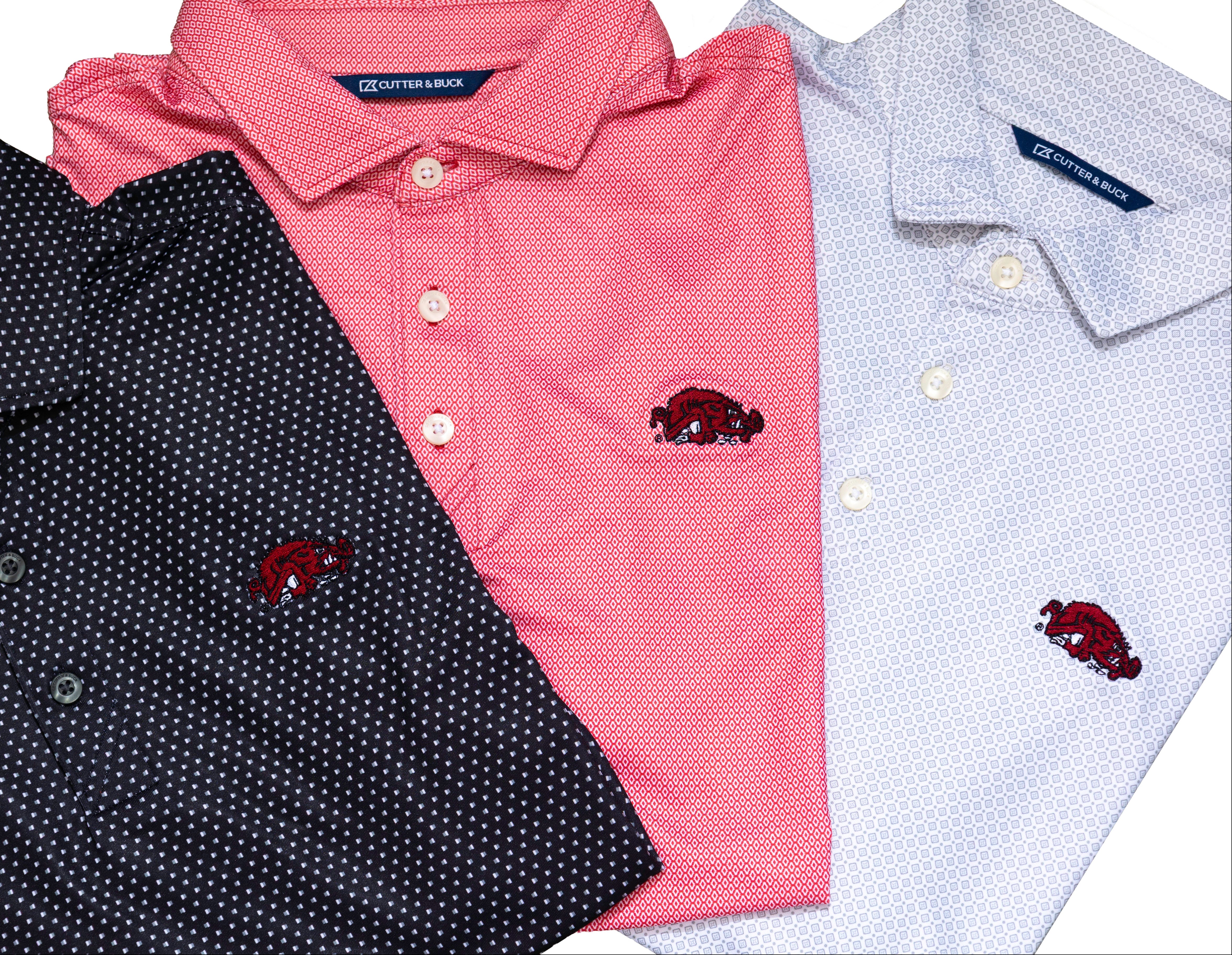 Three folded short-sleeve polo shirts shown on a white background: a dark black shirt with small white dots, a red shirt, and a light grey shirt with a subtle white dot pattern. Each shirt has a small embroidered red Razorback basktball logo on the chest.