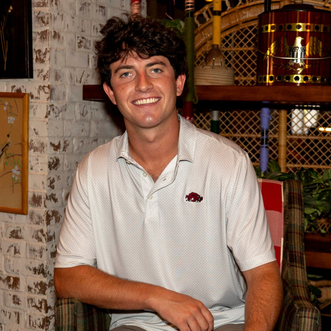 Close-up of a white patterned polo shirt with a red embroidered Arkansas Razorbacks Slobbering Hog logo on the chest 